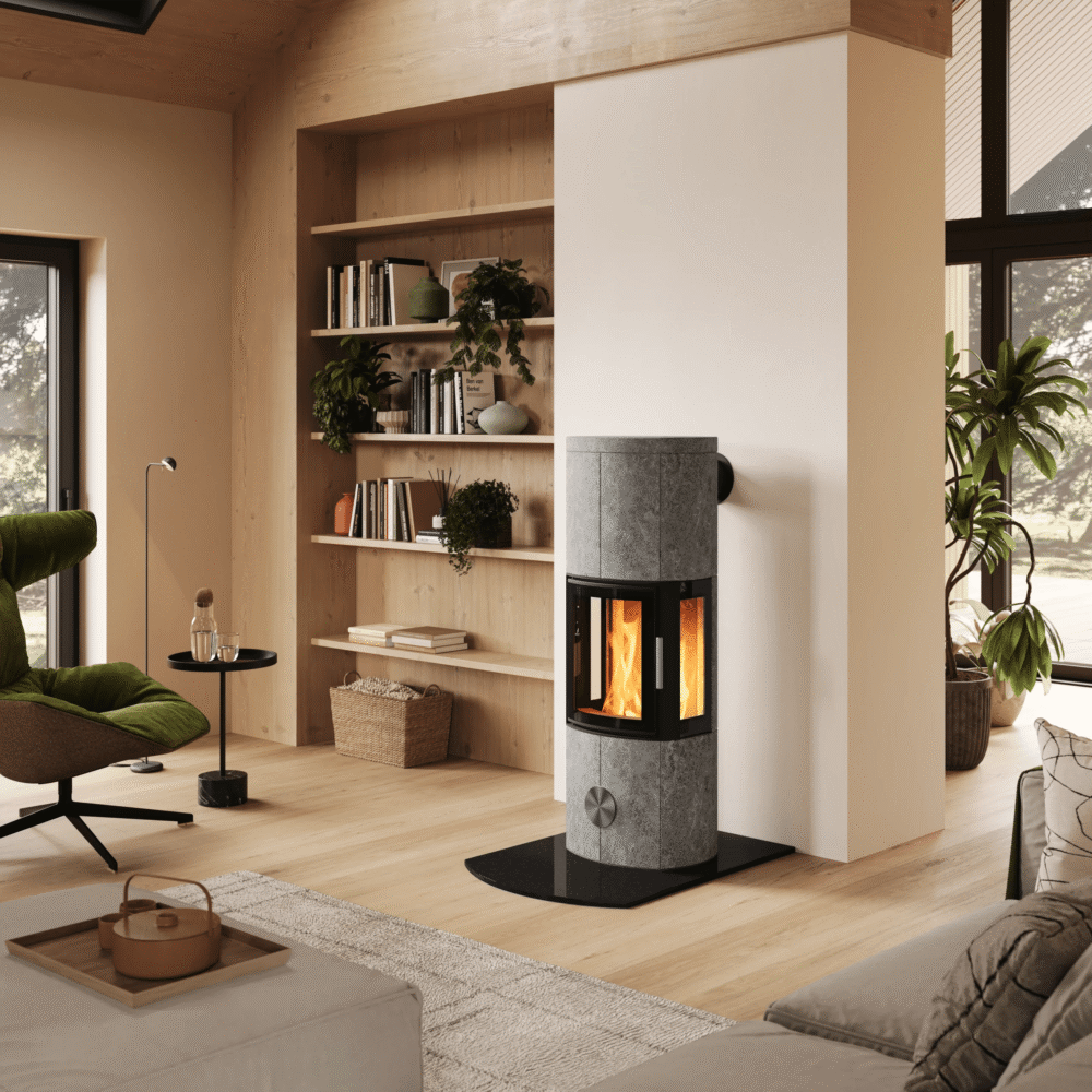Una stufa pietra ollare moderna collocata al centro di un interno scandinavo luminoso, con scala in legno, zona salotto e servizio da caffè in primo piano.